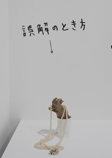 牛島光太郎の作品『組み合わせの方法』。日用品を組み合わせたモノと壁に油性ペンで言葉（文字）を書いた作品。